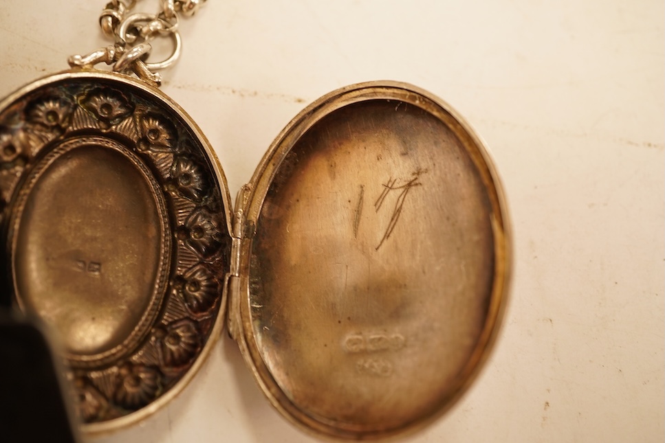 A late Victorian embossed and engraved oval silver locket, 42mm, on a later white meta belcher link chain, together with an Edwardian silver and hardstone inlaid pill box, now with pendant mount.